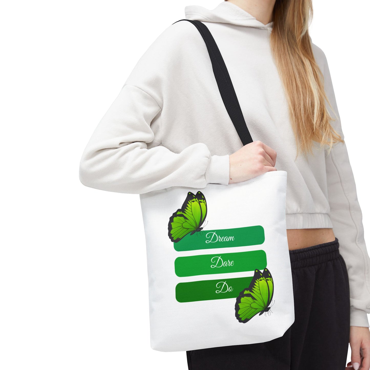 Woman carrying Elegant white Dream, Dare & Do tote bag with black handles, featuring a motivational design with butterflies and a green-toned background. This durable 100% polyester tote is perfect for students, professionals, or nature lovers. Available in sizes 13"x13", 16"x16", 18"x18". Luminous Gem Designs.