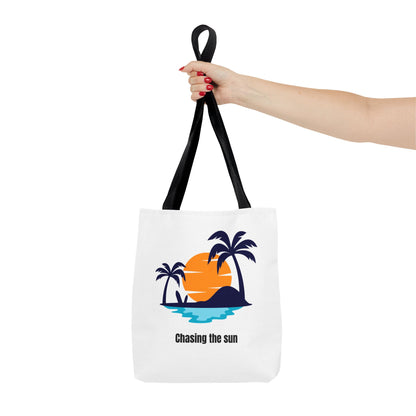 Hand holding Chasing the Sun tote bag in white with black handles, featuring a tropical palm tree design. This durable 100% polyester tote is perfect for summer adventures, beach trips, or grocery runs. Available in sizes 13"x13", 16"x16", 18"x18". Luminous Gem Designs.