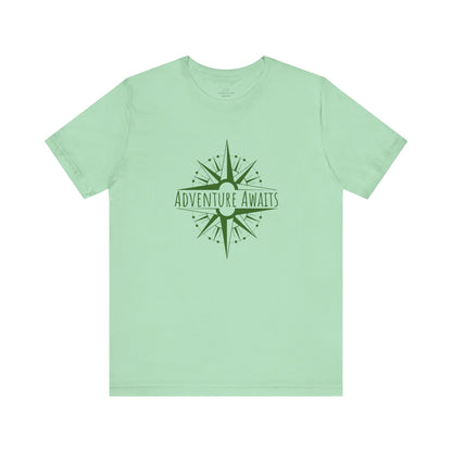 Mint green "Adventure Awaits" T-shirt featuring an earthy-toned compass print. A must-have for nature lovers, hikers, and wanderers. Sizes: XS, S, M, L, XL, 2XL, 3XL. Luminous Gem Designs.